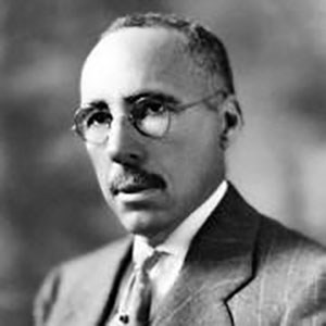 A black and white photo of a person in a suit with glasses