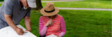 two people in hats sit outdoors looking at sketchbooks