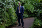 A person in a blue business suit stands surrounded by green vegetation