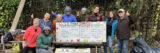 A group of people poses at a compost bin in a community garden
