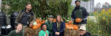 A group of six people poses with orange pumpkins and bales of hay