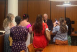a group of people huddle over a cabinet looking at a book inside a room with wood paneling