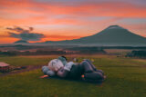A large statue lies looking at the sky in a green field at sunset