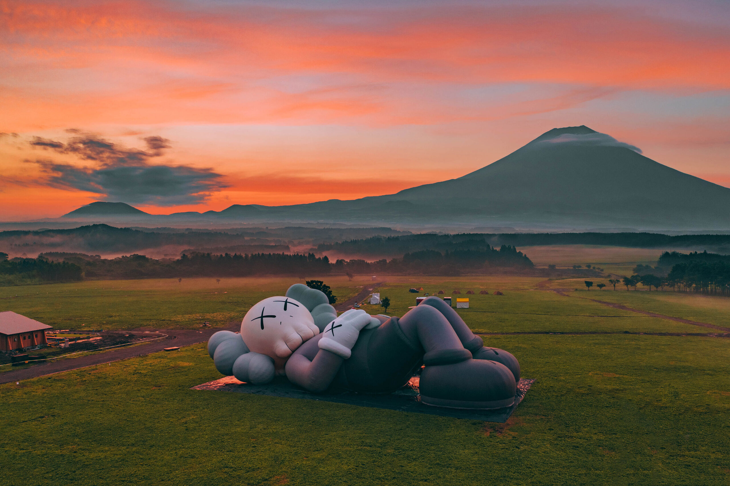 A large statue lies looking at the sky in a green field at sunset