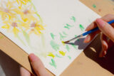 A person paints a watercolor painting of green and yellow flowers