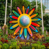 A large rainbow-hued sculpture of a flower sits in a lush conservatory