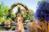Two people photograph each other in front of a large botanical peace sign installation