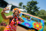 A person in a pink and orange dress takes a selfie in front of a colorful blue van