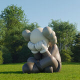 A large gray sculpture of a clown sits in a sunny green field