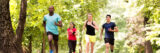 A group of four people runs through a sunny green forest