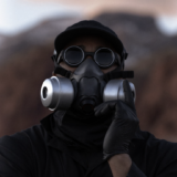 A person in a gas mask and black gloves poses for a photo