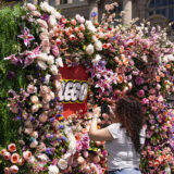 A person photographs a large wall of flowers with the LEGO logo in the center
