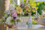 A white bottle of champagne set next to a pastel bouquet of flowers