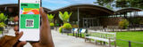A person holds up a smartphone with a QR code in a sunny outdoor garden