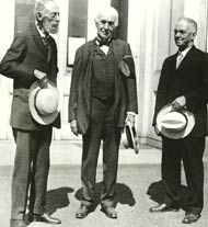 A black and white photo of three people in suits standing outside on a sunny day