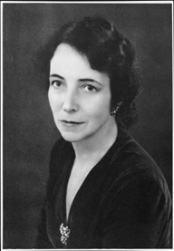 A black and white photo of a person wearing a black blouse and short-cropped dark hair