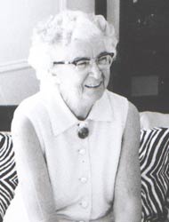 A black and white photo of a person with white hair, wearing a white shirt and glasses