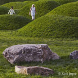 Two people walk through a lush, hilly field of green grass