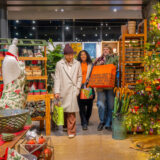 Three people pick gifts as they walk through a warmly decorated holiday shop display
