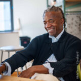 A person in a navy blue sweater sits in a brightly lit workspace