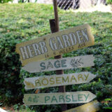 A garden sign listing herbs like sage, rosemary, and parsley