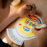 A child makes a mask with a paper plate and markers
