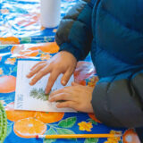 A child creates an herbarium specimen by gluing a green conifer stem to a piece of paper