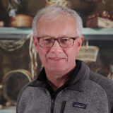 A person in a zip-up sweater and glasses poses for a photo
