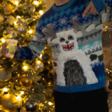 A person in a blue and white sweater celebrates among twinkling holiday lights while drinking a cocktail
