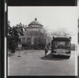 A black and white photo of a bus dropping people off outside a conservatory dome