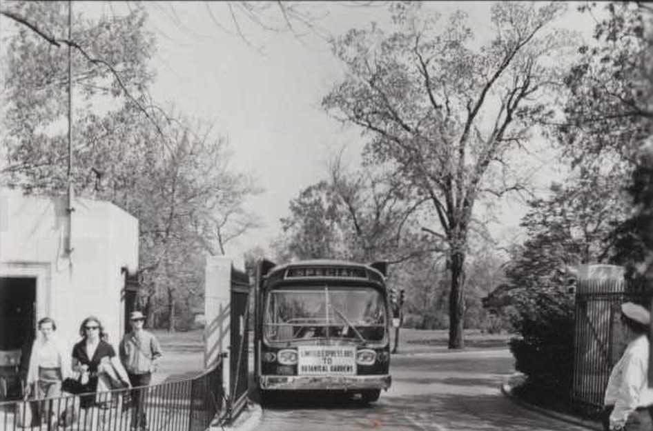 A black and white photo of a bus passing through a gate
