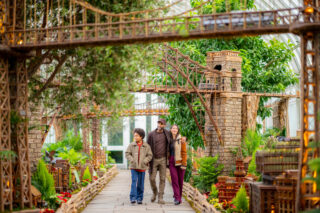 A family, with two parents and a child, walk through the Holiday Train Show and admire the displays.