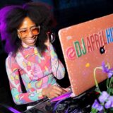 A person in a colorful pink and blue shirt, and orange sunglasses, DJs at a laptop