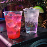 A pair of cocktails in tall cups, sitting on a speaker
