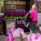 A person observes a colorful newsstand covered in flowers