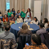 A group of people gather around a round table for a conference