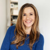 A person with long blonde hair, wearing a blue sweater, poses for a photo