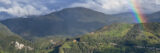 A green, mountainous landscape under a blue sky, with a colorful rainbow visible
