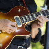 A person plays a golden-brown electric guitar