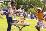 A parent and child play a game of jenga on a sunny day on the lawn