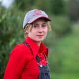 A person in a red shirt and gray hat poses for a photo outdoors