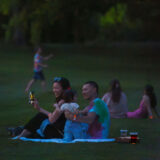 A family sits on a picnic blanket during an evening event