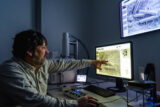 A person in a darkened laboratory points at a computer screen