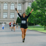 A person holds their hands above their head as they run with a group down a long path