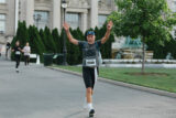 A person in a hat raises both arms while jogging along