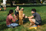 Three people sit on a lawn playing giant Jenga