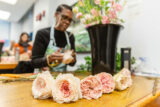 A person in a black shirt and denim apron arranged pink flowers in a bouquet