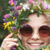 A person in sunglasses poses with a flower crown around their face