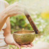 A person runs a wooden rod around the rim of a metal singing bowl
