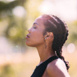A person in a black tanktop meditates outdoors on a sunny day